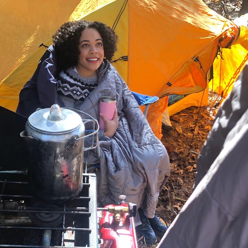 Woman keeping warm with blanket in front of tent.
